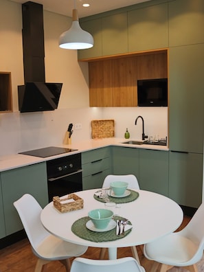 A modern kitchen with a white table set for two, a built-in oven, and a microwave above the counter. - Vista Alegre Valley - Laurissilva, Nature & Peace in Madeira Island (São Vicente)