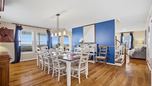 Comedor con mesa de madera y sillas blancas, pared decorativa azul y una escalera que sube a otro nivel.