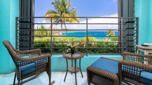 Ein Balkon mit Korbmöbeln, einem kleinen Tisch und Blick auf einen tropischen Strand und Ozean.