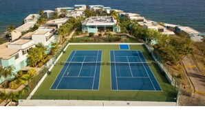 Eine Vogelperspektive eines Küsteneigentums mit Tennisplatz, umliegenden Gebäuden und Blick auf den Ozean.