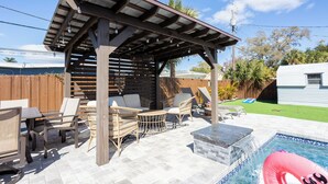 A covered outdoor seating area with wicker furniture, a pool with a floating ring, and a wooden pergola. - Peaceful 4-bedroom house with AC and Heated Pool in charming Largo Florida (Largo)