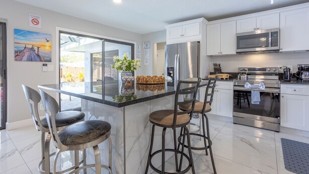 A modern kitchen with white cabinets, stainless steel appliances, and a central island with bar stools. - Peaceful 4-bedroom house with AC and Heated Pool in charming Largo Florida (Largo)