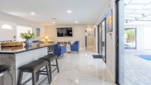 A modern kitchen with a marble countertop, bar stools, and a large TV. - Peaceful 4-bedroom house with AC and Heated Pool in charming Largo Florida (Largo)