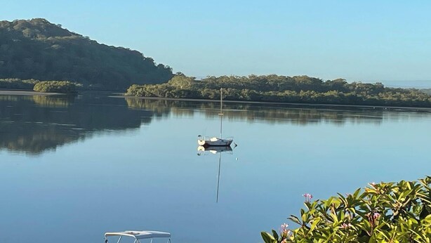 A calm lake with a boat anchored in the center, surrounded by lush greenery and hills in the background. - Room-salt and Sea Renity On Milton (Russell Island)