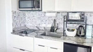 A modern kitchen with white cabinets, a stainless steel microwave, a built-in toaster, a coffee maker, and a sink with a faucet. - 29th floor ocean view Waikiki Hawaiian Monarch (Honolulu)