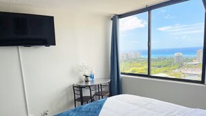 A hotel room with a bed, a TV mounted on the wall, a small table with chairs, and a window with a city view. - 29th floor ocean view Waikiki Hawaiian Monarch (Honolulu)