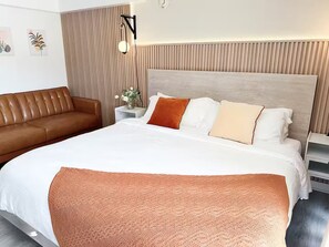 Ein modernes Hotelzimmer mit einem großen Bett, einer braunen Ledersofa, einem Nachttisch mit Blumenvase und einer Wandlampe.