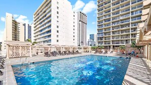 A rooftop swimming pool with lounge chairs and a view of surrounding high-rise buildings. - Waikiki Seaside Luxury King Condo with Balcony (Honolulu)