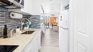A modern kitchen with a stone backsplash, white cabinetry, and a built-in oven. - Waikiki Seaside Luxury King Condo with Balcony (Honolulu)