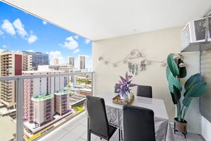 Un balcón con vistas a la ciudad, una mesa de comedor con sillas, una planta en maceta y un aire acondicionado fijado a la pared.
