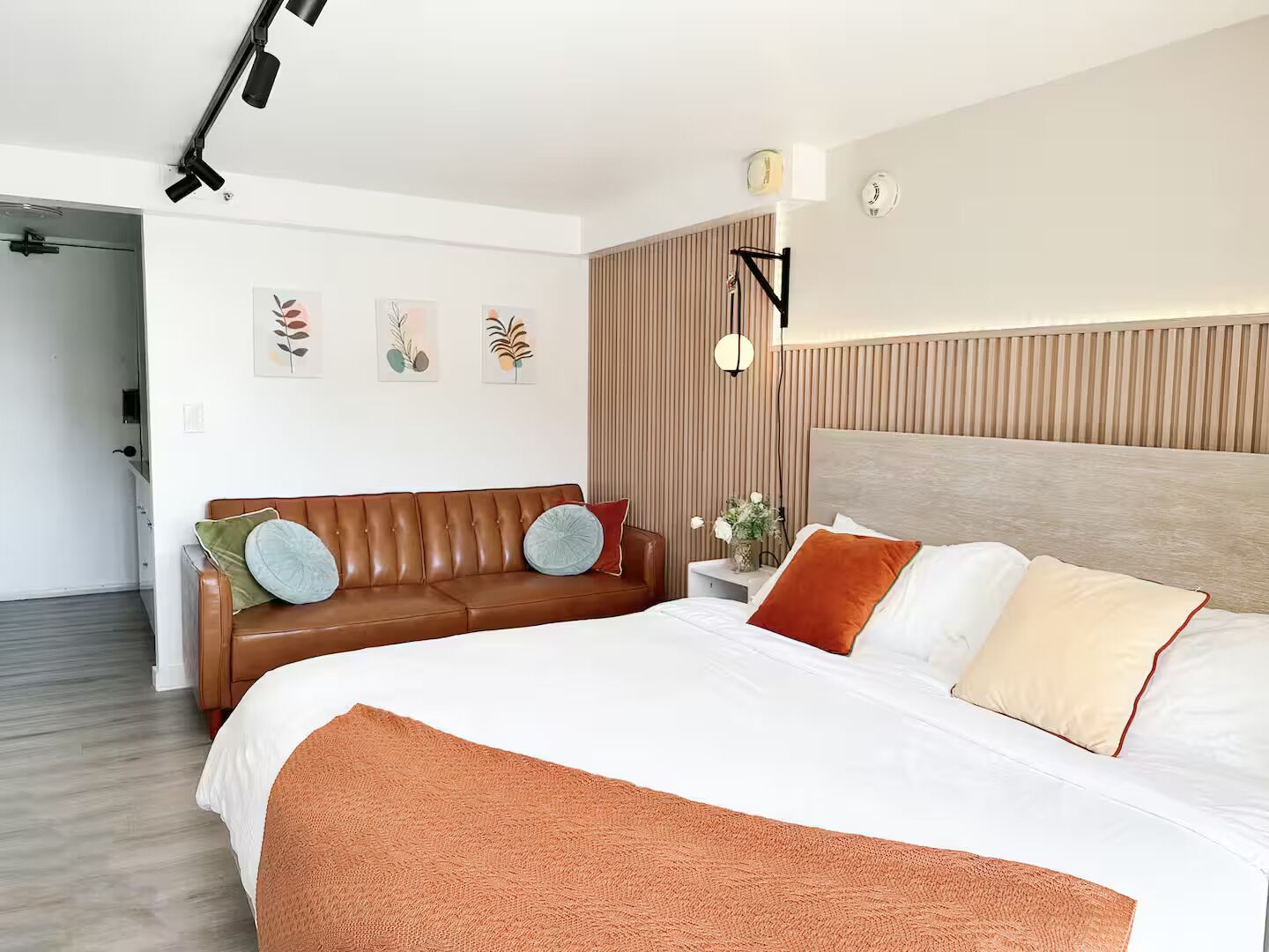 A modern bedroom with a large bed, a brown leather sofa, and a bedside table with a lamp.