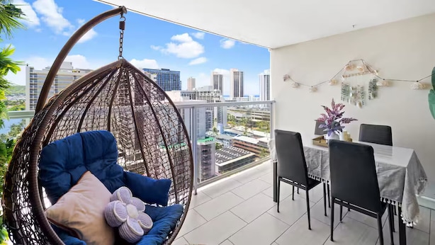 A balcony with a hanging chair, dining table, chairs, and a view of the cityscape. - Waikiki Seaside Luxury King Condo with Balcony (Honolulu)