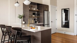 Une cuisine moderne dotée d’un îlot central, de meubles en bois foncé, d’appareils électroménagers en acier inoxydable et de luminaires suspendus.