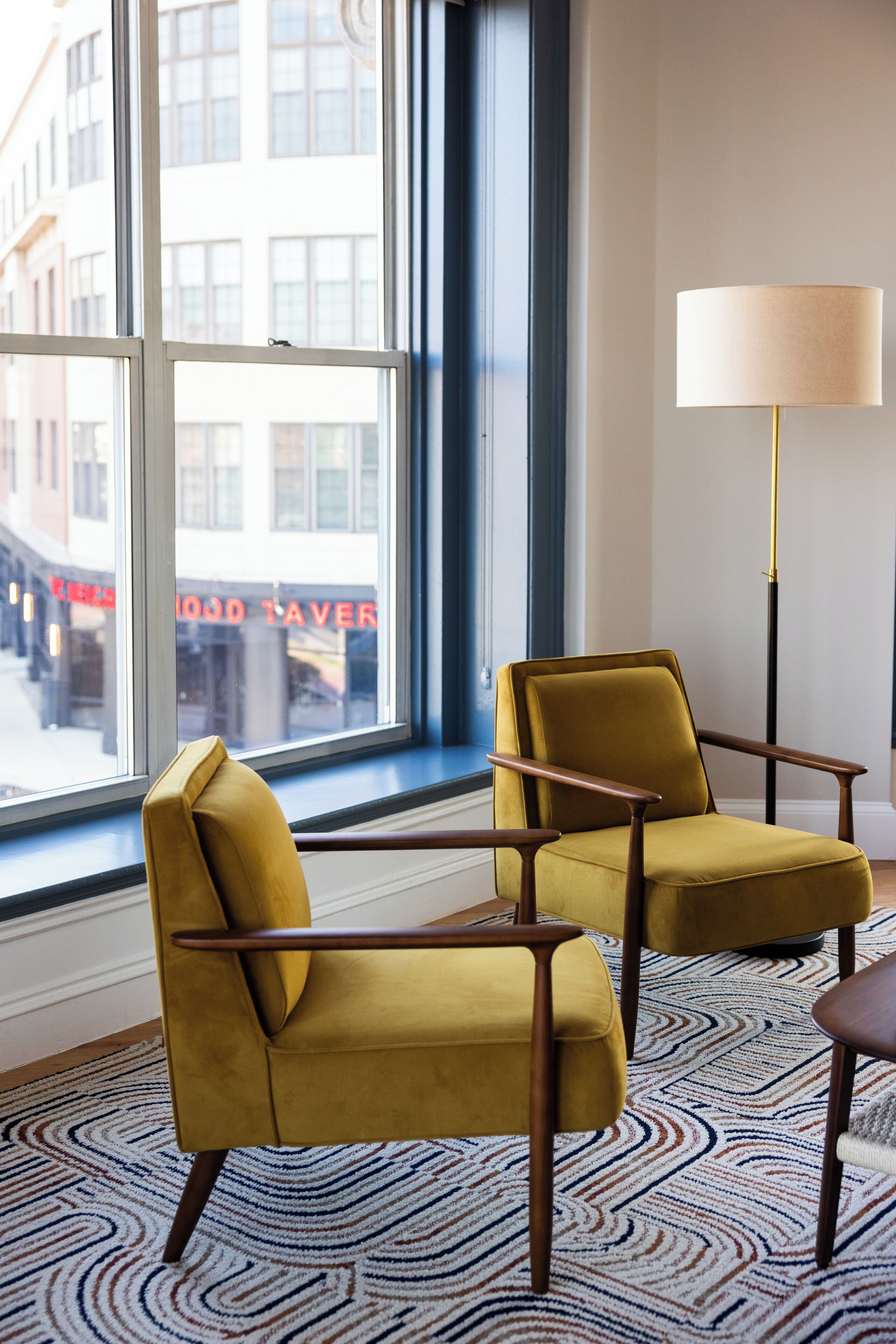A room with two yellow armchairs, a floor lamp, and a patterned rug.