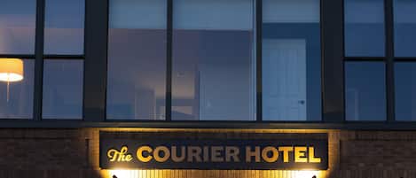 El Hotel Courier con un cartel sobre la entrada, ventanas grandes y luces colgantes.