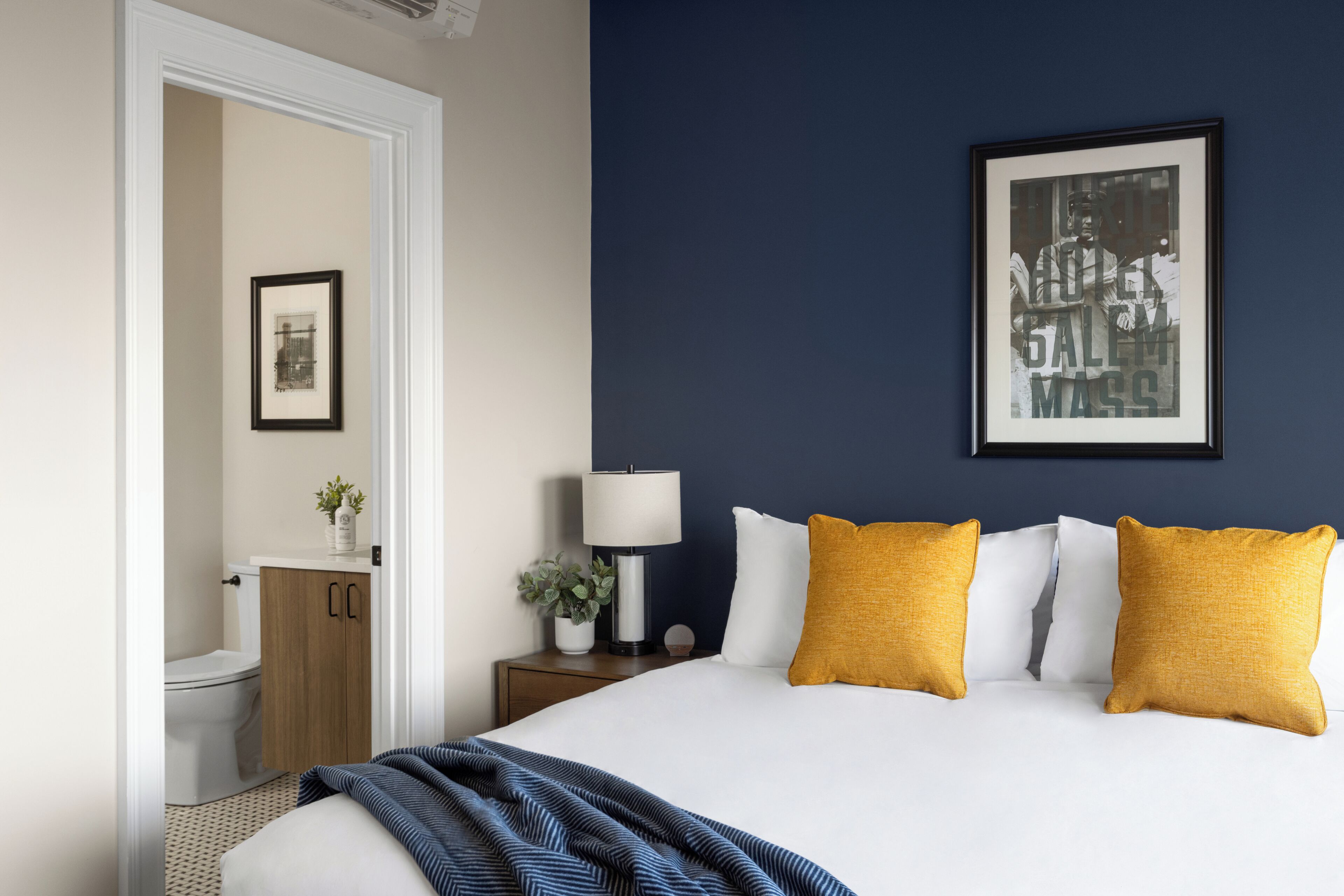 A hotel room with a bed, a nightstand, a lamp, and a framed picture on the wall.