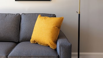 A sofa with a mustard-colored pillow, a framed picture on the wall, and a floor lamp.