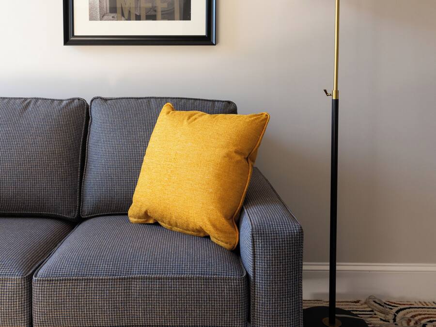 A sofa with a mustard-colored pillow, a framed picture on the wall, and a floor lamp.