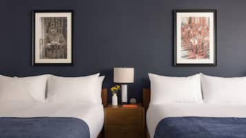 Habitación de hotel con dos camas, una mesita de noche con lámpara y un jarrón de flores, y dos cuadros en la pared.