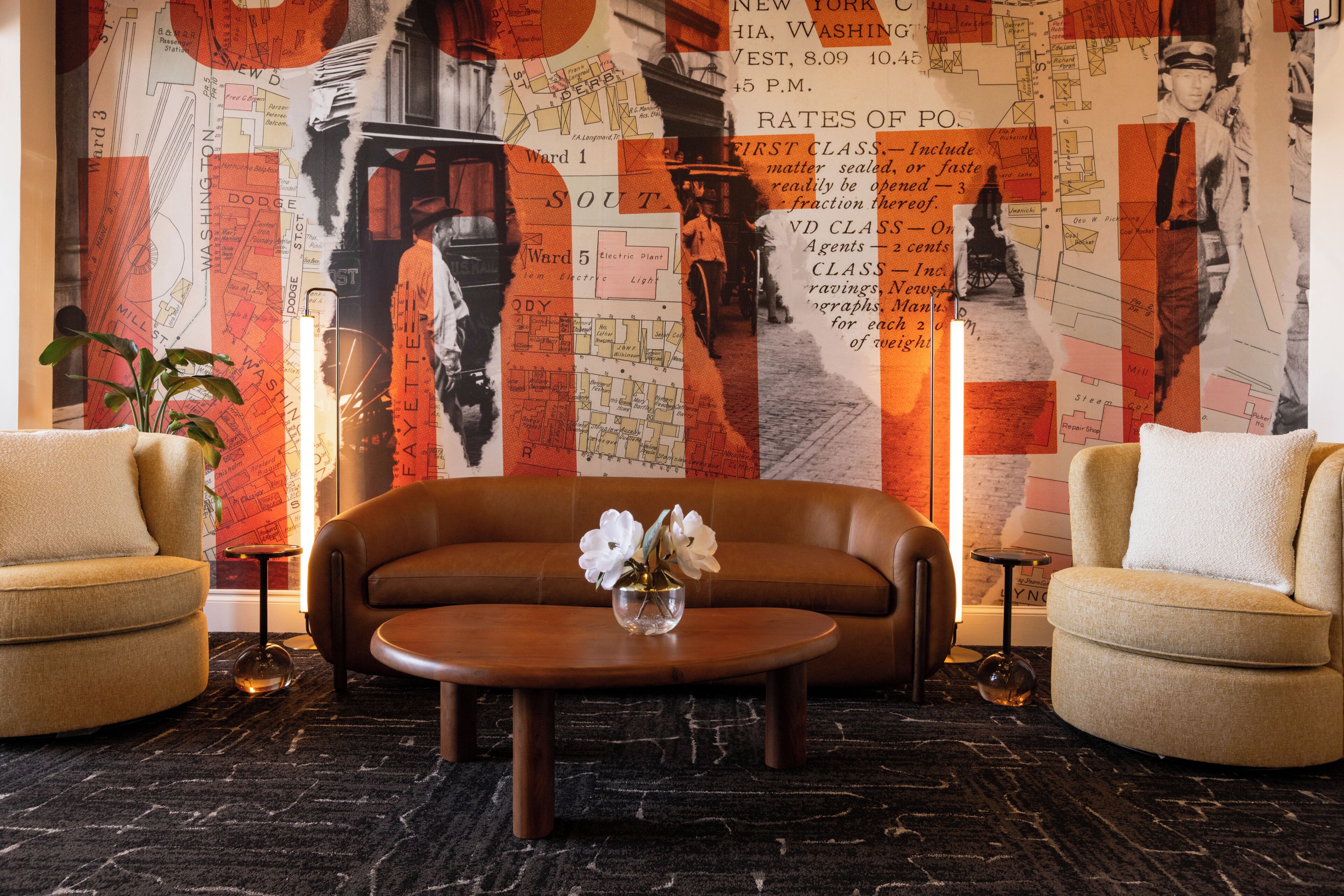 A modern living room with a sofa, two armchairs, a coffee table, and a decorative wall with maps and vintage photographs.