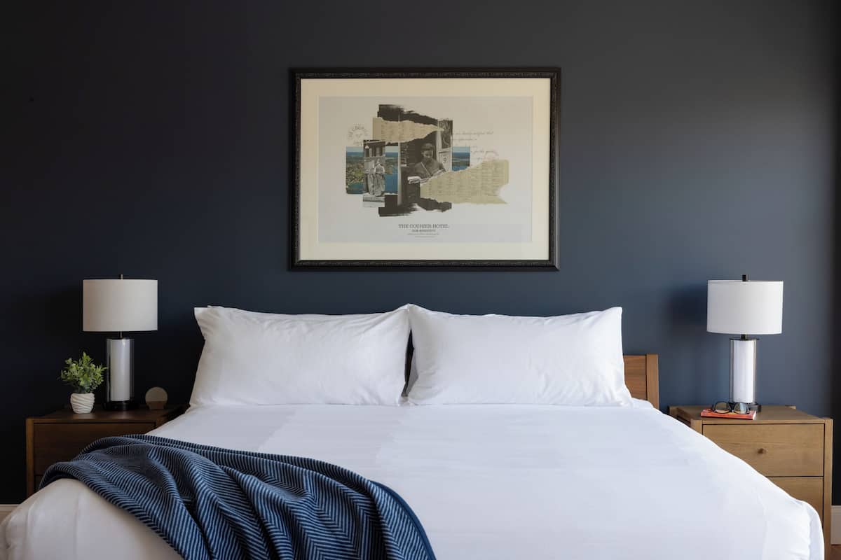 Un letto rifatto con lenzuola bianche, due comodini con lampade e un quadro appeso al muro.
