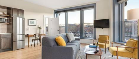 Een moderne woonkamer met een grijze bank, gele fauteuils, een salontafel en uitzicht op de stad door grote ramen.