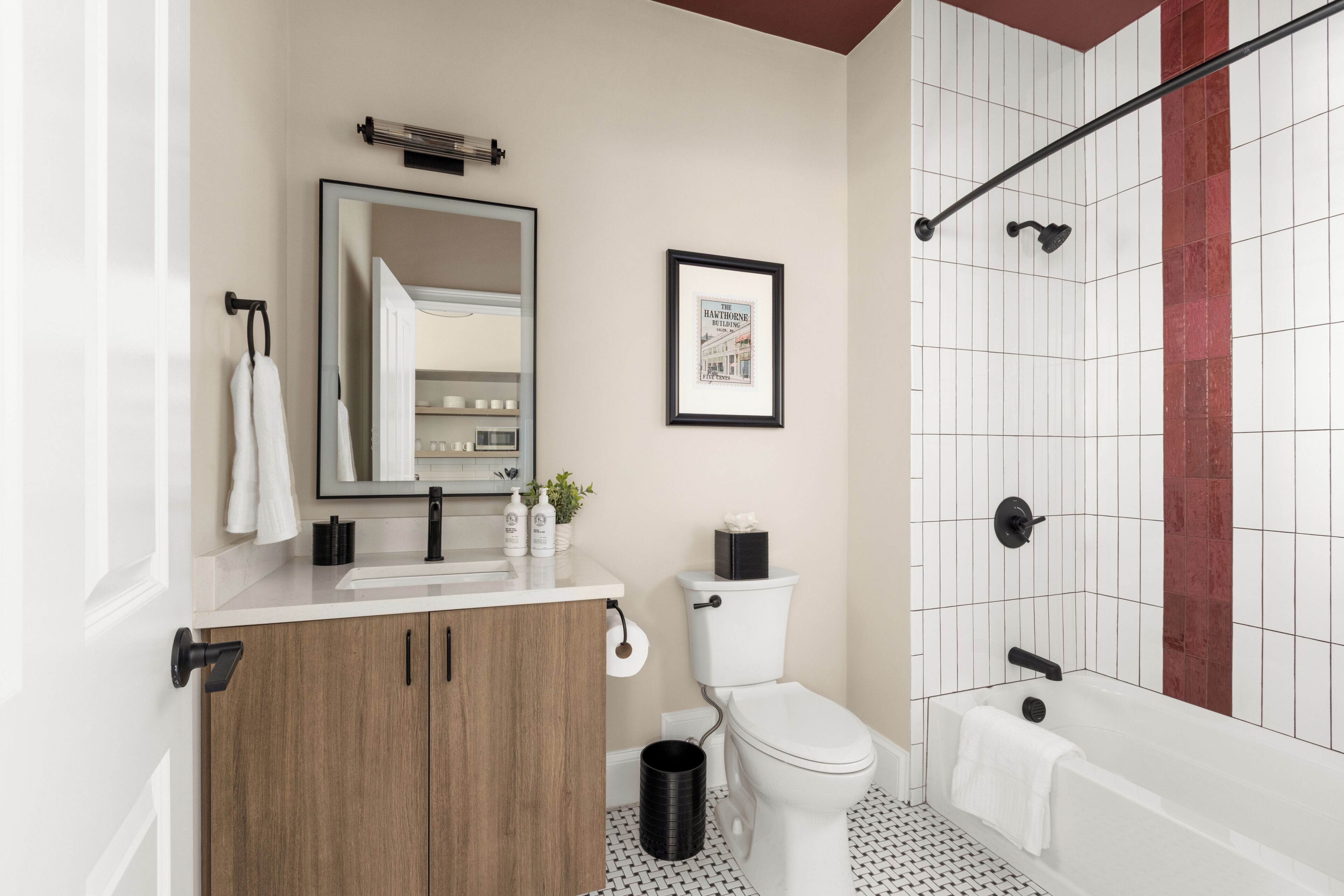 A modern bathroom with a toilet, sink, mirror, framed picture, and a bathtub.