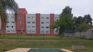 A swimming pool with stone tiles, surrounded by a grassy area and a building in the background. - UNIVERSIFLAT Ponta Grossa. (Ponta Grossa)