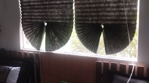 A room with a window covered by a striped curtain, a small table with a plant, and a sofa with cushions. - UNIVERSIFLAT Ponta Grossa. (Ponta Grossa)