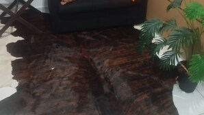 A black sofa with orange and patterned cushions, a dark brown rug, and a potted plant with green leaves. - UNIVERSIFLAT Ponta Grossa. (Ponta Grossa)