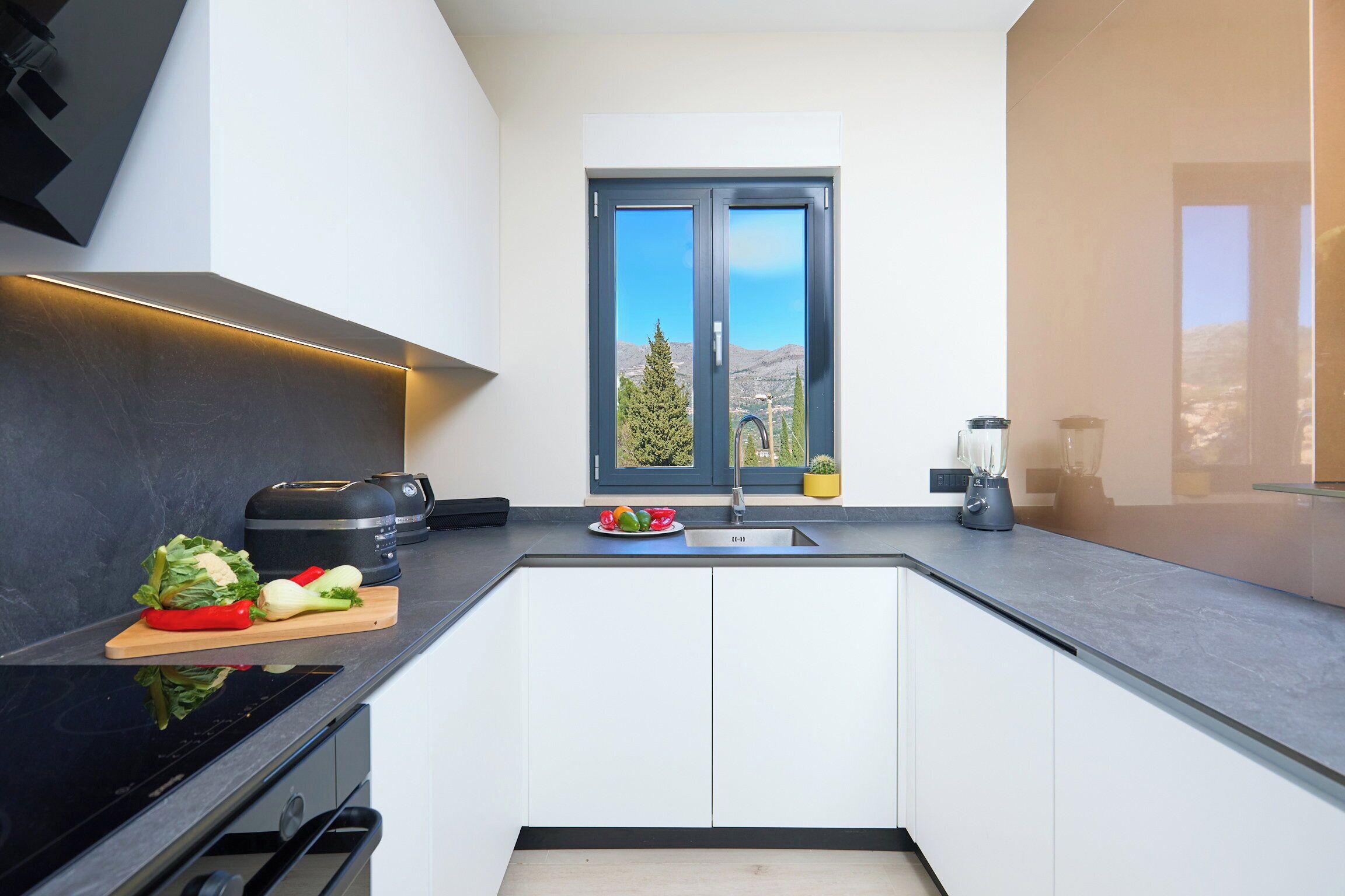 Una cocina moderna con horno empotrado, un lavamanos y un ventanal con vistas a las montañas.