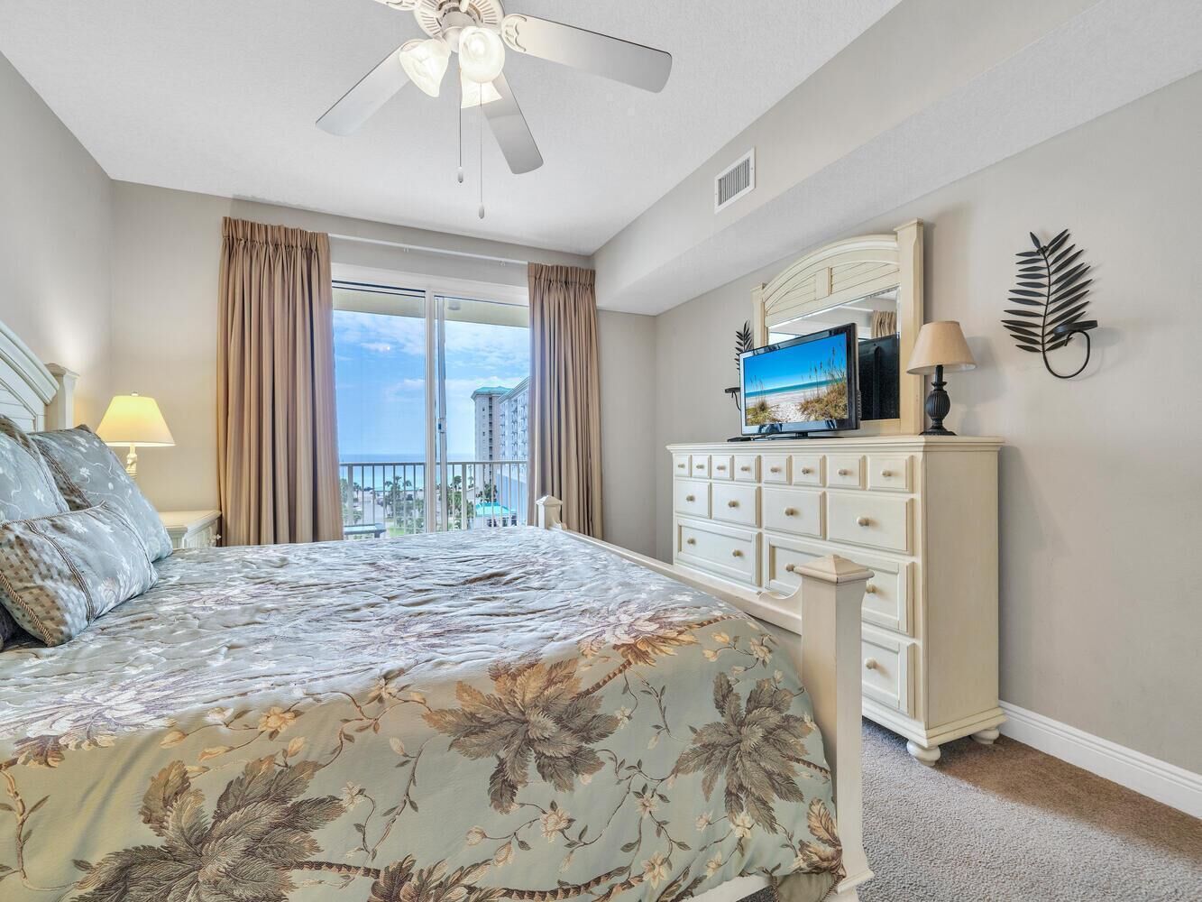 A bedroom with a bed, a dresser, a TV, and a balcony with curtains.