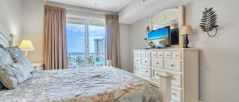 A bedroom with a bed, a dresser, a TV, and a balcony with curtains.