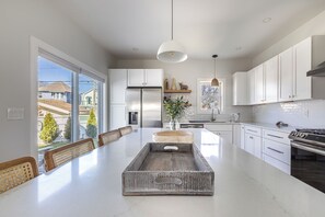 A modern kitchen with a large island, white cabinetry, and a view to the outside.