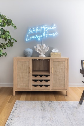 Un armario de madera con cestas de mimbre, una escultura de coral y un letrero de neón que dice 'Walnut Beach Luxury House'.