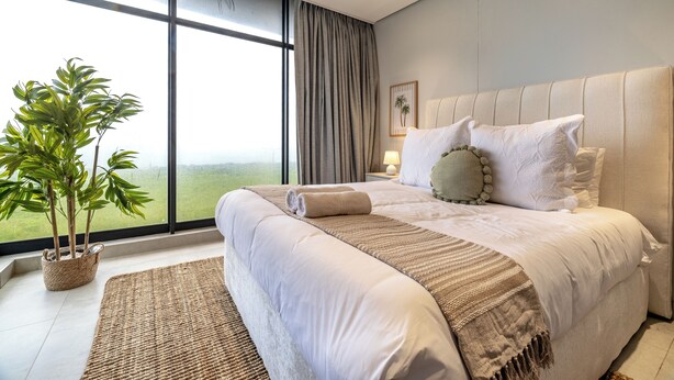 A modern bedroom with a large bed, a potted plant, and a view of the outdoors. - Chic Umhlanga Studio | Walk to Beaches (Umhlanga)