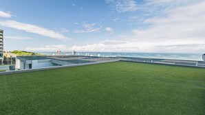 A rooftop terrace with artificial grass, a view of the sea, and modern buildings in the background. - Chic Umhlanga Studio | Walk to Beaches (Umhlanga)