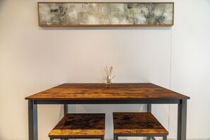 Een houten tafel met twee banken, een kleine vaas met rietstengels en een groot abstract schilderij aan de muur.