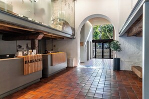 A reception area with a wooden counter labeled "BARRACKS," a tiled floor, and an arched doorway leading outside. - Modern City Pad with Great Walkability (Cape Town)