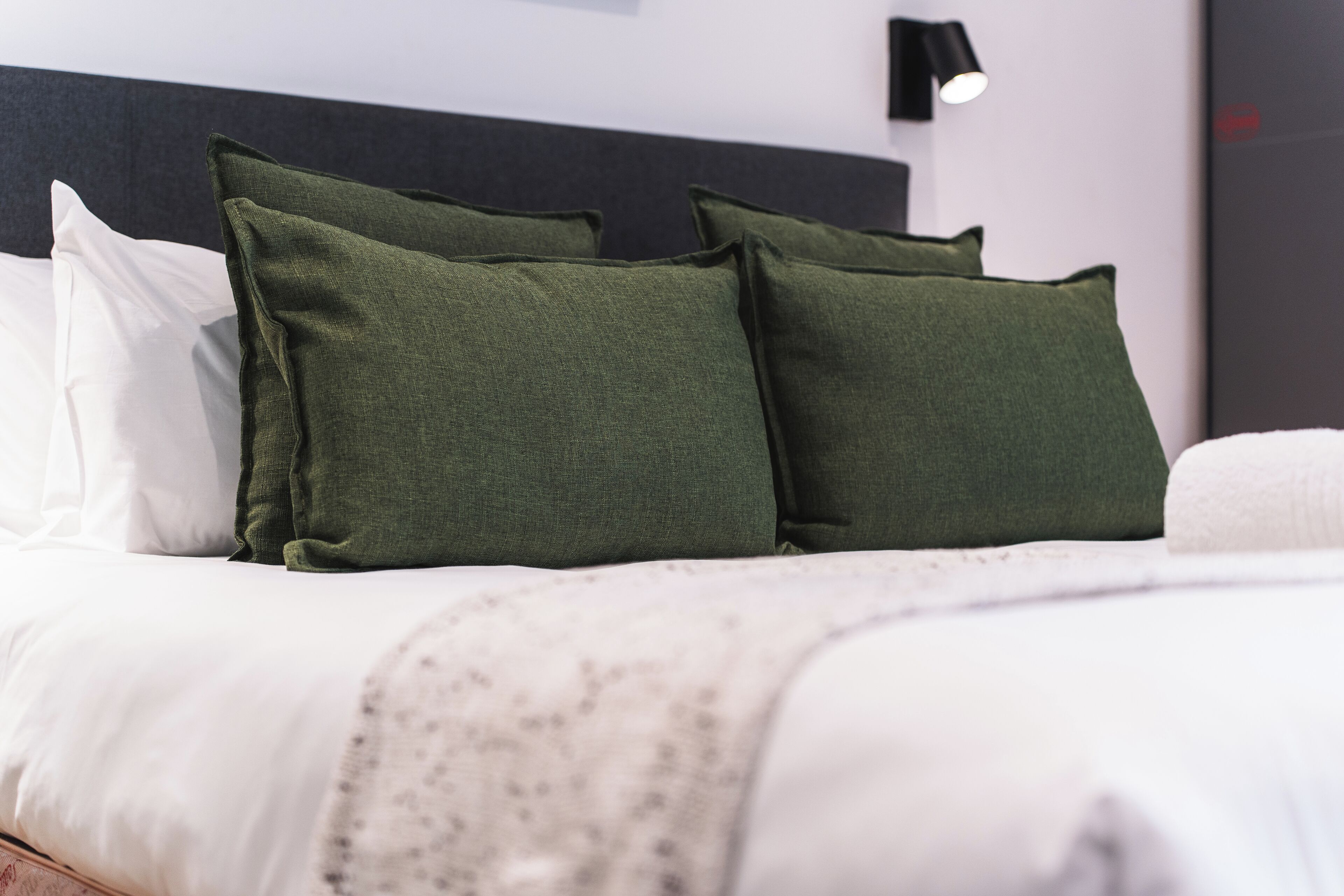 A neatly made bed with green and white pillows, a dark headboard, and a small bedside lamp.