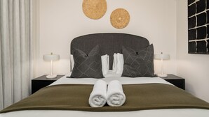 Una habitación de hotel moderna con una cama grande, dos mesitas de noche con lámparas, un cabecero oscuro y decoración mural tejida.