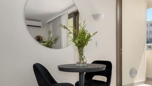 Una habitación moderna con una mesa redonda, dos sillas negras, una planta en maceta, un espejo circular y vistas al exterior.