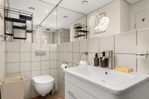 A modern bathroom with a white sink, toilet, and mirror. There are shelves with toiletries and a trash bin. - Dolce Vita | Modern Sea Point Retreat (Cape Town)