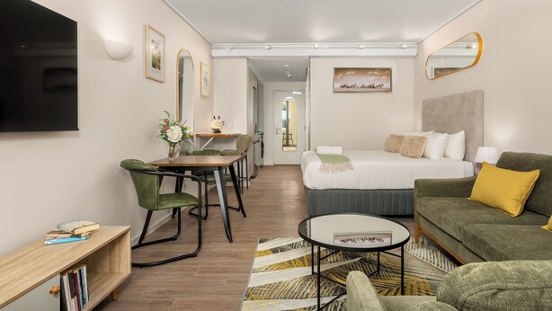 Una habitación de hotel moderna con cama, sofá, zona de comedor y televisión.