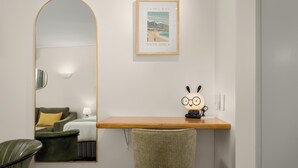 Habitación de hotel con un espejo grande, un cuadro enmarco de Camps Bay, Sudáfrica, un escritorio de madera, una silla y una lámpara.