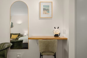 Habitación de hotel con un espejo grande, un cuadro enmarco de Camps Bay, Sudáfrica, un escritorio de madera, una silla y una lámpara.