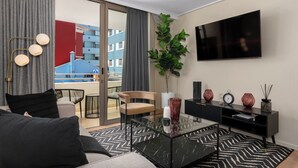 Un salon moderne avec un canapé, une table basse en verre, un fauteuil, un téléviseur et un balcon offrant une vue sur les immebles.