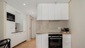 Une cuisine moderne avec des meubles blancs, un four encastré et un plan de travail sur lequel se trouve une machine à café.