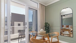 Ett modernt vardagsrum med ett glasbord, trästolar, en stor spegel och utsikt över staden genom en skjutdörr i glas.