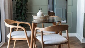 En matplats med ett bord i glas, två trästolar med gråa kuddar och en flätad korg med en vit vas.